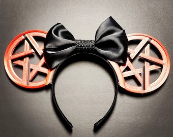 May include: Black bow with rhinestones on a headband with two orange star-shaped ears.