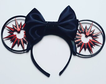 May include: Black Minnie Mouse ears with a red and black starburst design. The ears are decorated with a black satin bow.