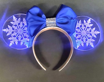 May include: A pair of light blue LED Minnie Mouse ears with a blue bow and snowflake designs. The ears are made of clear acrylic and light up with blue LEDs.