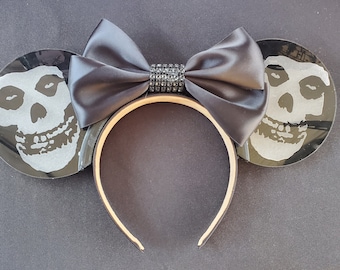 May include: Black and white skull-shaped Mickey Mouse ears with a black satin bow and a rhinestone embellishment.