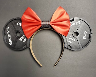 May include: Black weight plates with the text "Grumpy's Gym 45 LBS" on each side, with a red satin bow and a rhinestone embellishment in the center.