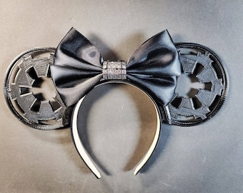 May include: Black mouse ears with a black satin bow and a silver rhinestone embellishment. The ears are shaped like the Star Wars Imperial symbol.