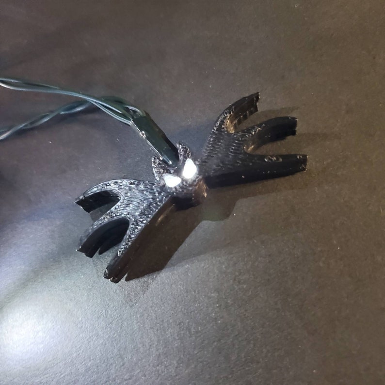 May include: A black 3D printed bat with white glowing eyes, hanging from a string of lights.