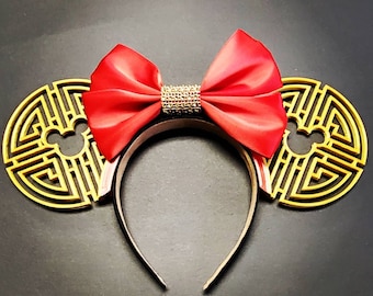 May include: Red satin bow with gold glitter accents on a black headband with gold Mickey Mouse ears. The ears are decorated with a gold Chinese knot design.