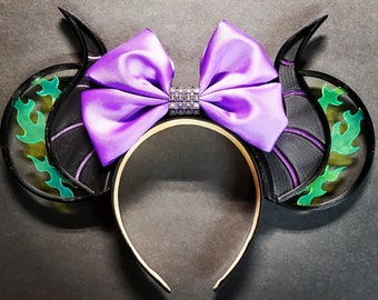 May include: Purple and black headband with a large purple bow and a rhinestone center. The headband is decorated with green and black flames.