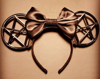 May include: A pair of black and silver mouse ears with a large black satin bow. The ears are shaped like a starburst.