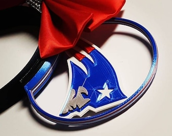 May include: Red and white bow with rhinestones on a black headband with a blue, white, and red 3D printed design of a football team logo.