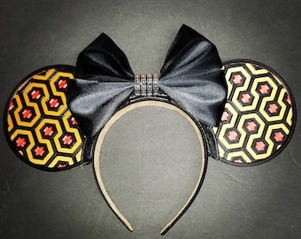 May include: Black satin bow headband with yellow and red patterned fabric ear pieces. The pattern is a geometric design of interlocking hexagons.