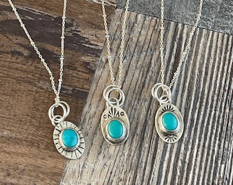 May include: Three silver necklaces with turquoise stones set in oval pendants. Each pendant has a different design around the stone.