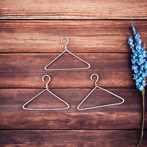 May include: Three silver wire hangers on a brown wooden background. The hangers are arranged in a triangular shape.