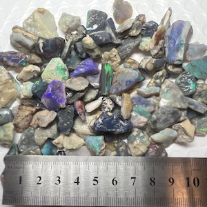 May include: A pile of raw opal stones in shades of blue, green, purple, and grey. The stones vary in size and shape, with a ruler at the bottom for scale. The ruler measures up to 30 cm.