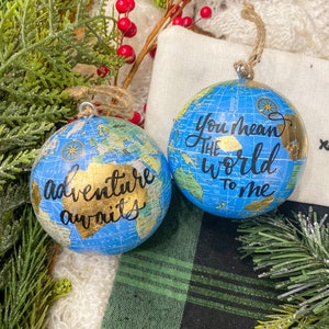 May include: Two blue globe ornaments with gold accents. One ornament says "Adventure awaits" and the other says "You mean the world to me".