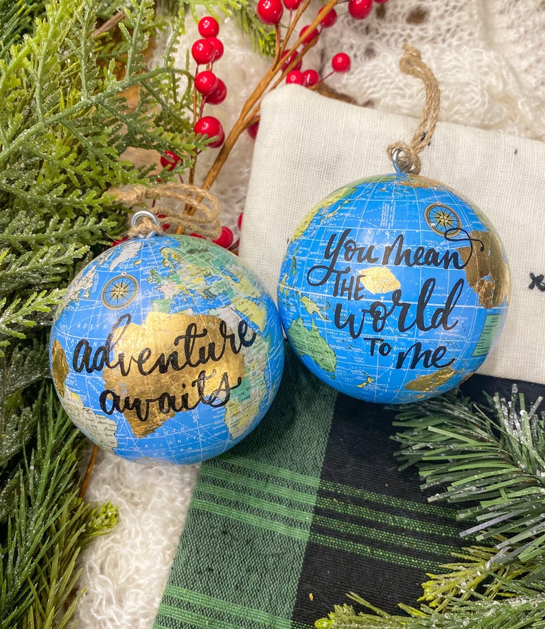 May include: Two blue globe ornaments with gold accents. One ornament says "Adventure awaits" and the other says "You mean the world to me".