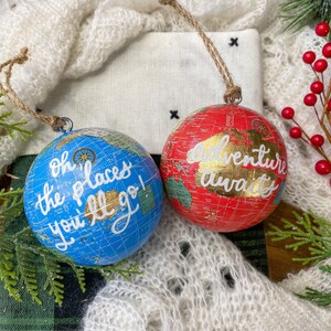 May include: Two globe-shaped Christmas ornaments with a vintage map design. One is blue with the text "Oh the places you'll go!" and the other is red with the text "Adventure awaits".