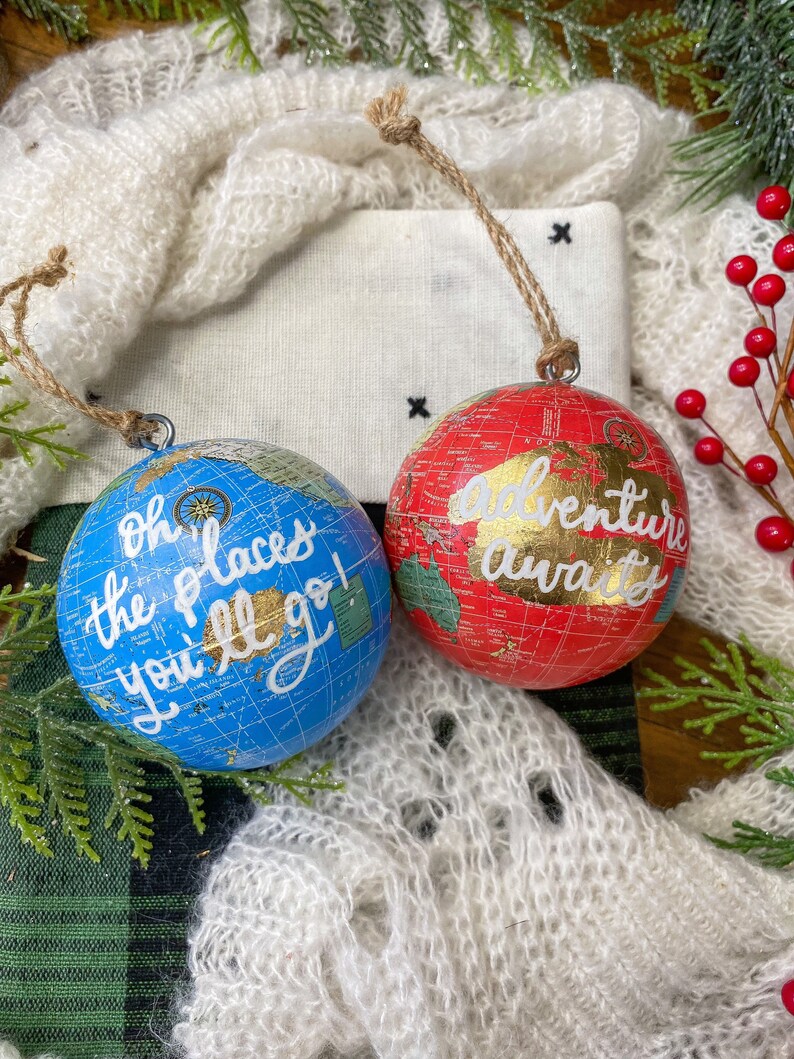 May include: Two globe-shaped Christmas ornaments with a vintage map design. One is blue with the text "Oh the places you'll go!" and the other is red with the text "Adventure awaits".
