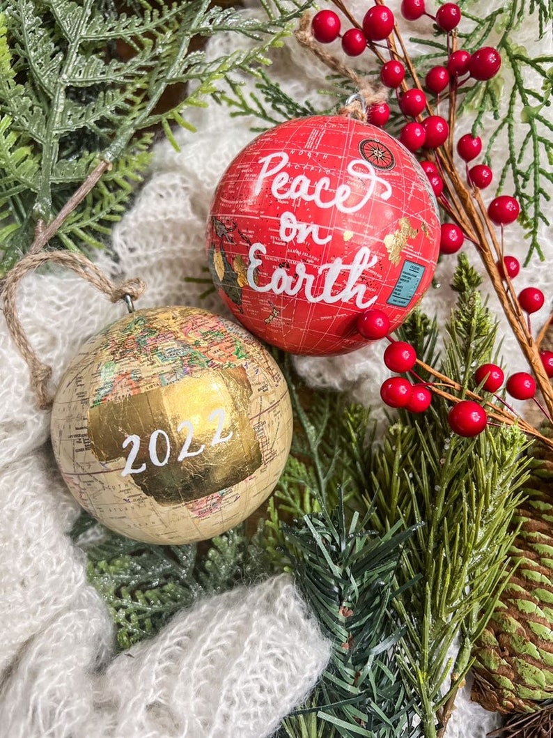 May include: Two globe-shaped Christmas ornaments. One is red with the text "Peace on Earth" and the other is gold with the year "2022" written on it.