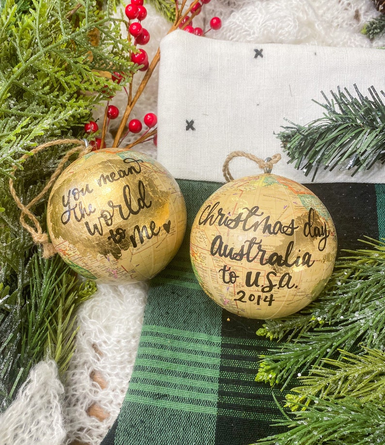 May include: Two gold globe ornaments with black calligraphy. One ornament says "You mean the world to me" with a heart. The other ornament says "Christmas day Australia to U.S.A. 2014".