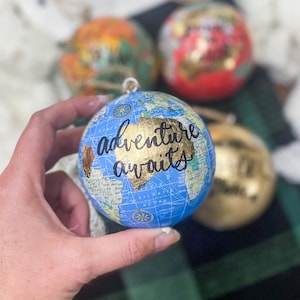 May include: Blue globe Christmas ornament with a gold map and the words "adventure awaits" written in black.