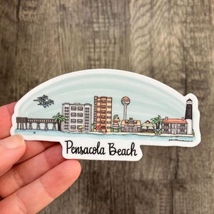 May include: A sticker featuring a colorful illustration of Pensacola Beach, Florida. The design includes a pier, buildings, and a lighthouse, with the words "Pensacola Beach" in a script font.