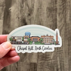 May include: A sticker featuring a stylized skyline of Chapel Hill, North Carolina, with buildings, trees, and a water tower. The text "Chapel Hill, North Carolina" is written in a script font below the skyline. The sticker has a white border and a light blue background.