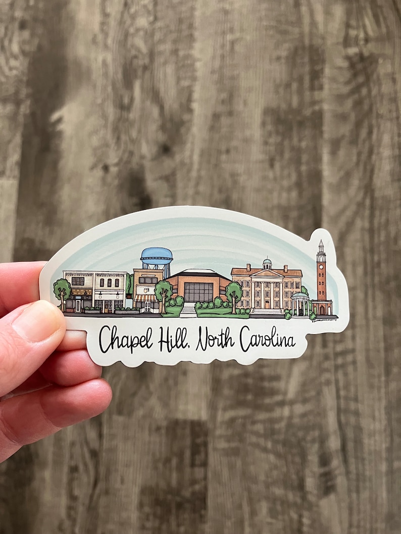 May include: A sticker featuring a stylized skyline of Chapel Hill, North Carolina, with buildings, trees, and a water tower. The text "Chapel Hill, North Carolina" is written in a script font below the skyline. The sticker has a white border and a light blue background.