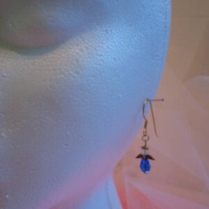 Op de afbeelding: Een paar gouden oorhangers met een blauwe kristallen hanger. De oorhangers zitten op een witte mannequinkop.