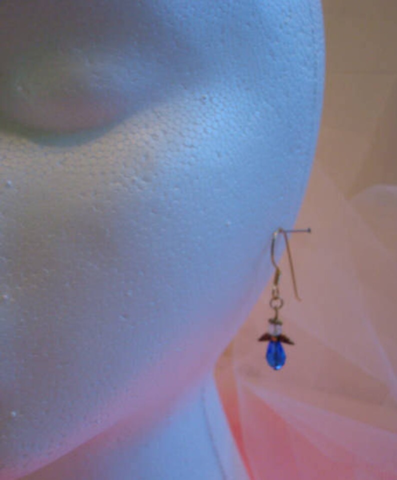 Op de afbeelding: Een paar gouden oorhangers met een blauwe kristallen hanger. De oorhangers zitten op een witte mannequinkop.