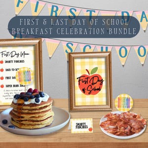 Op de afbeelding: Een ontbijt-celebratiepakket met ingelijste menu's, pannenkoeken, spek en decoratieve banners. De ingelijste menu's luiden "First Day Menu" en "First Day of School". De pannenkoeken zijn belegd met bessen en siroop.