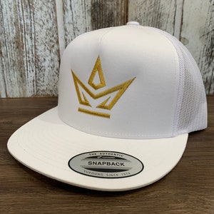 Puede incluir: Gorra de camionero blanca de malla con un logotipo de corona dorada y el texto "THE AUTHENTIC YUPOONG SNAPBACK YUPOONG SINCE 1974" en la etiqueta.