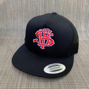 Puede incluir: Gorra de b&eacute;isbol negra con un dise&ntilde;o bordado en rojo y una parte trasera de malla. La gorra tiene una etiqueta blanca con el texto "The Authentic Snapback Yupoong Since 1974".
