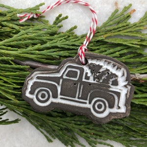 Op de afbeelding: Een bruine keramische kerstversiering in de vorm van een pick-up truck met een kerstboom in de laadbak. De truck is wit omrand en heeft witte wielen.