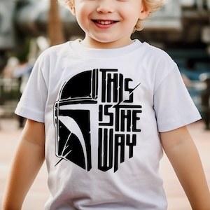 May include: A white t-shirt with a black graphic of a Mandalorian helmet and the text "This is the way".