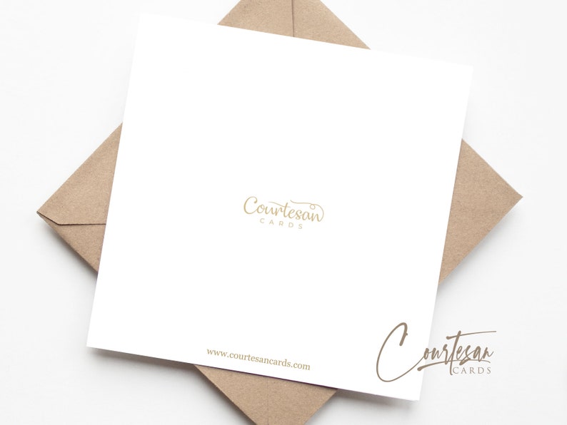 May include: A white card with the text "Courtesan Cards" in gold lettering. The card is sitting on a brown envelope.