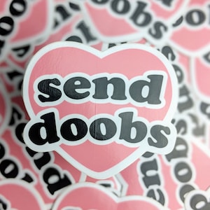 Puede incluir: Una pegatina rosa en forma de corazón con el texto "send doob" en letras negras. La pegatina está rodeada de otras pegatinas similares.