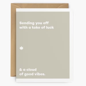 May include: A greeting card with a light brown background and white border. The card reads "Sending you off with a toke of luck & a cloud of good vibes." A small white cannabis leaf is also on the card. The card is in a brown envelope.