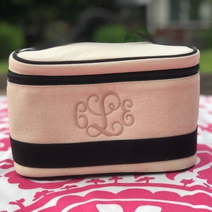 May include: A white canvas makeup bag with a black zipper and black trim. The bag has a monogrammed "L" in pink thread.