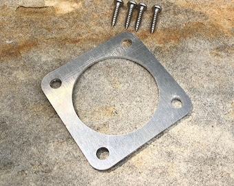 Può includere: Una piastra di montaggio quadrata in metallo color argento con un grande ritaglio circolare al centro e quattro fori più piccoli agli angoli, accompagnata da quattro piccole viti in metallo color argento con gambo filettato e testa piatta.