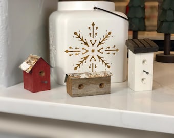 Può includere: Tre casette per uccelli in miniatura, una rossa, una bianca e una in legno, con una lanterna in ceramica bianca con un'incisione a forma di fiocco di neve sul davanti.