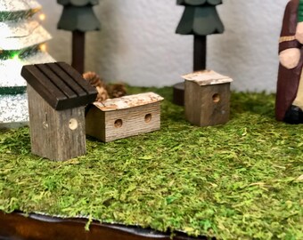 Può includere: Tre casette per uccelli in miniatura di legno, dipinte di marrone e bianco. Le casette per uccelli sono appoggiate su un letto di muschio verde.