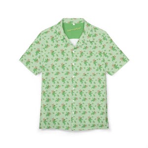 Puede incluir: Camisa verde claro con botones y un patrón repetido de ajolotes verdes con branquias rojas y pequeñas plantas. La camisa tiene cuello de campamento y el texto "Abirrrryygglgg!" en el cuello.