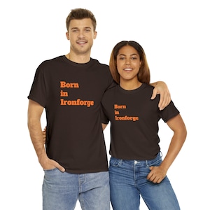 Puede incluir: Dos personas con camisetas marrones con el texto "Born in Ironforge" en naranja. La persona de la izquierda lleva pantalones vaqueros azules. La persona de la derecha lleva pantalones vaqueros azules.