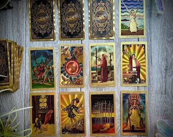 May include: A set of 10 tarot cards with gold foil accents. The cards feature illustrations of various figures and symbols, including a wheel of fortune, a fool, and a queen of wands. The cards are arranged in two rows of five.