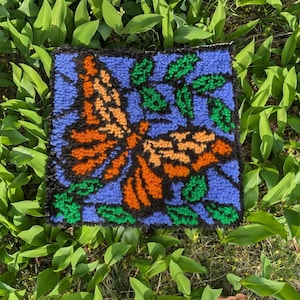May include: A colorful rug with a butterfly design. The butterfly is orange, brown, and black, and the background is blue with green leaves.