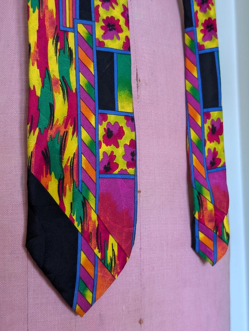 May include: A colorful silk tie with a geometric pattern featuring pink flowers, yellow, green, orange, and blue stripes. The tie has a black background.