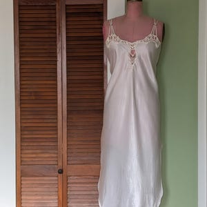 May include: A white satin slip dress with delicate lace detailing at the neckline and straps.