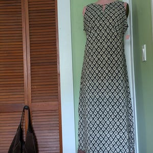 May include: A sleeveless floor-length dress featuring a repeating black and white geometric diamond pattern. The garment has a small keyhole cutout at the neckline and a decorative horizontal band with a brown and black border at the hemline.