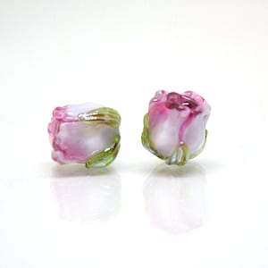 May include: Two pink and white glass rose beads with green leaves. The beads are small and delicate, and they would be perfect for making jewelry or other crafts.