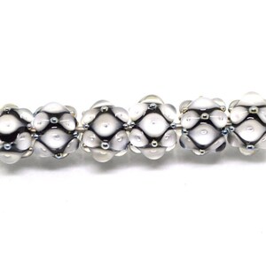 May include: Six white glass beads with a black and silver geometric pattern. The beads are strung on a silver wire.