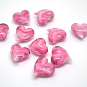 Peut inclure: Dix perles en verre en forme de c&oelig;ur de couleur rose avec des tourbillons blancs. Les perles sont &eacute;parpill&eacute;es sur une surface blanche.