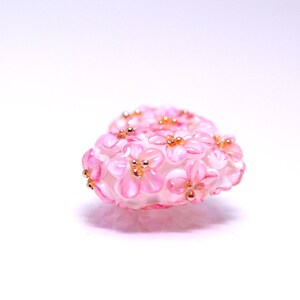 May include: A pink heart-shaped charm made of glass beads, with a design of small pink flowers with gold centers.